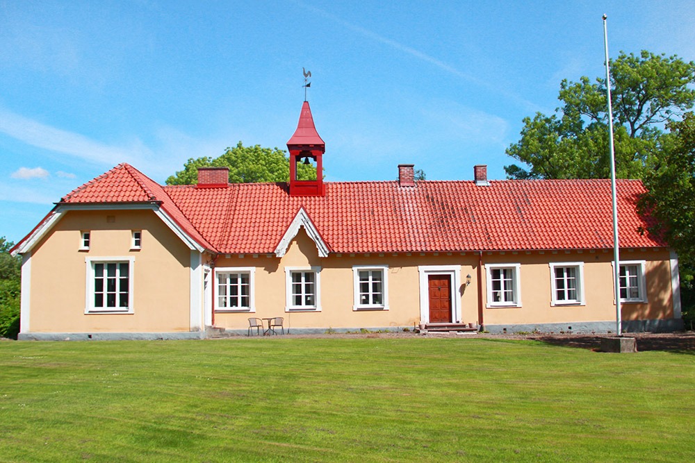 Gult bostadshus med rött tegeltak och liten klockpelare på taket.