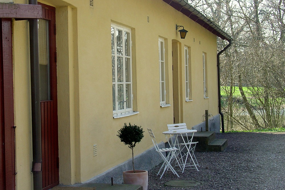Gult bostadshus i närbild med vita cafemöbler utanför.