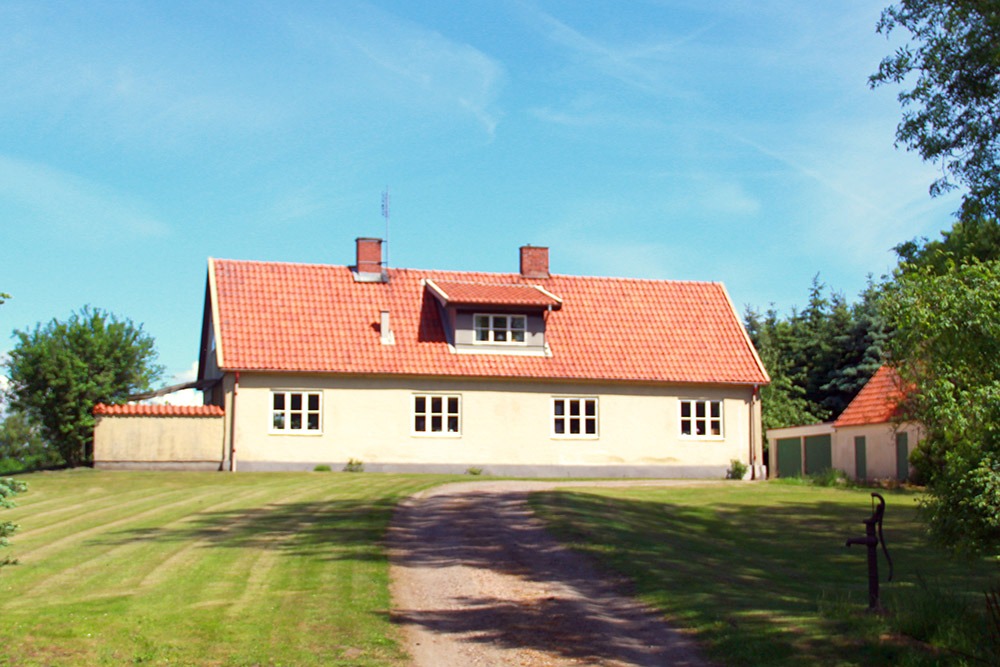 Gult bostadshus med gräsmatta och grusväg framför.