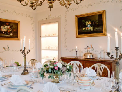 Elegant matsal med dukat bord, ljus, blommor och klassisk väggkonst.